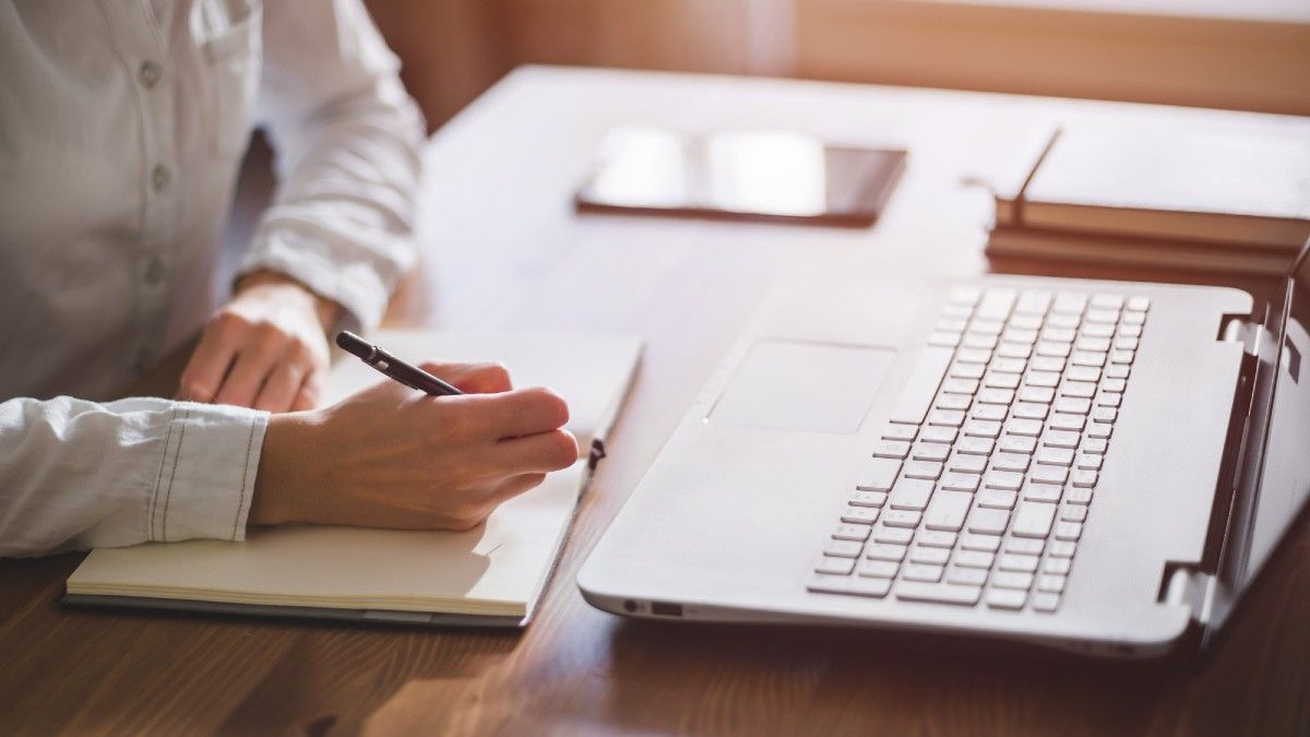 Individual writing down information in front of open laptop