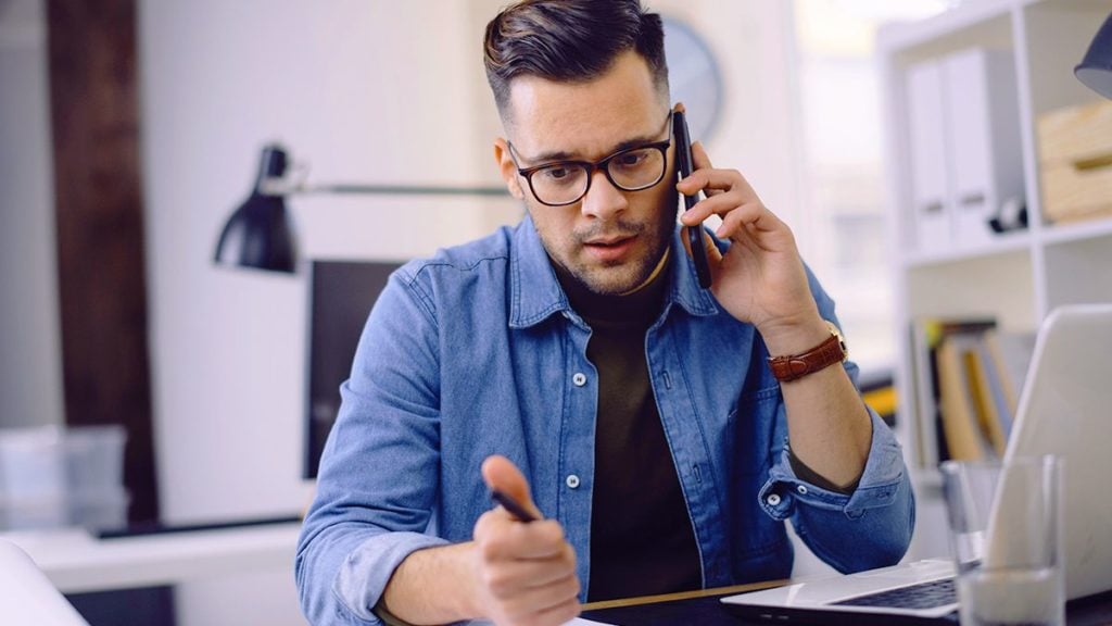 man with glasses on phone holding a pen with one hand and looking at copy of a w-3 form