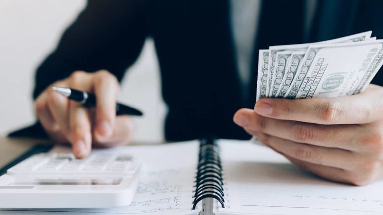 business owner using a calculator with one hand and holding cash in another