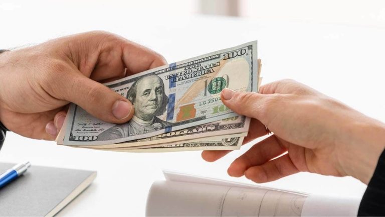 Someone handing a small stack of $100 bills to someone else