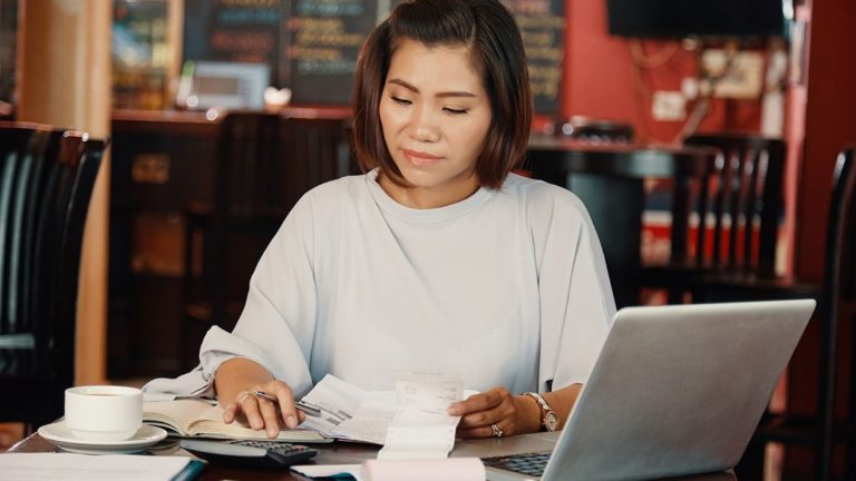 woman with short hair holding receipts and using calculator while updating her books