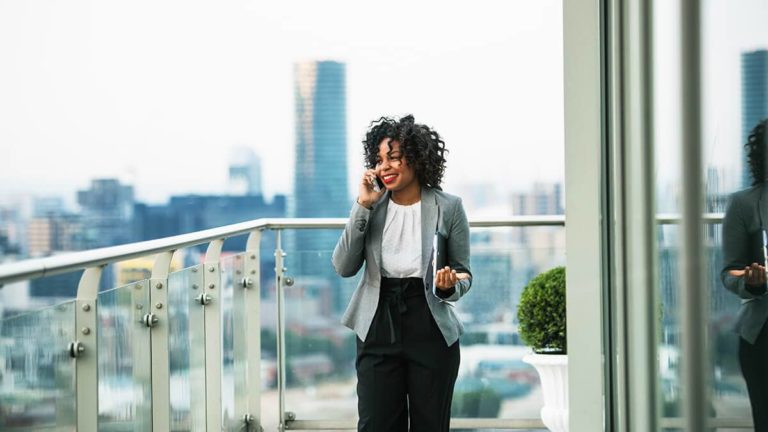 Corporate woman on the phone with the city in the background.