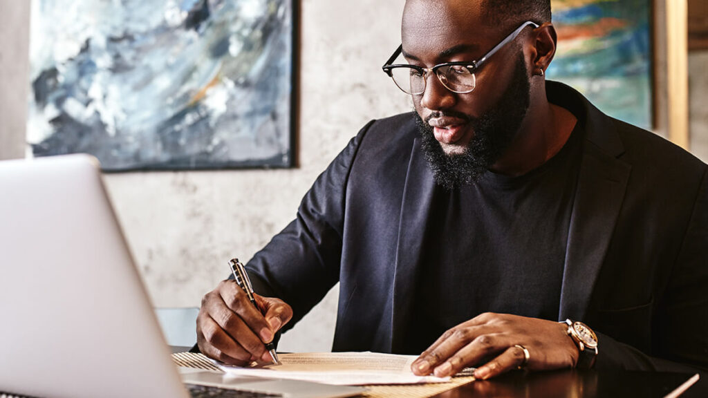 Man writing on a document and using a laptop.