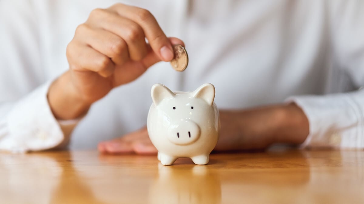 Business owner dropping money into a white piggy bank.