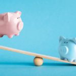 A pink and blue piggy bank on a seesaw.