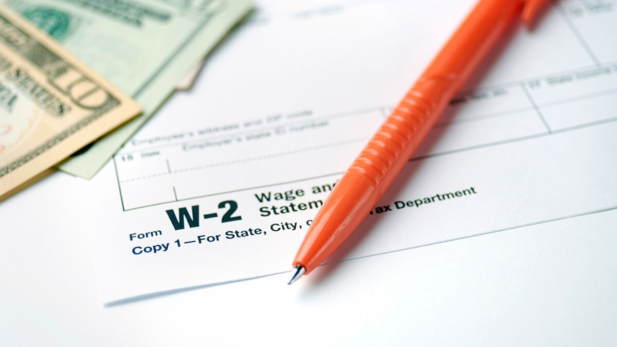 Form W-2, Wage and Tax Statement, with orange pen and money on top.