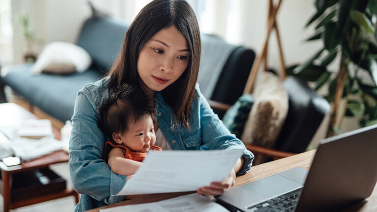 Woman preparing a balance sheet while holding baby.