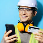 Smiling construction worker entering credit card information into phone.