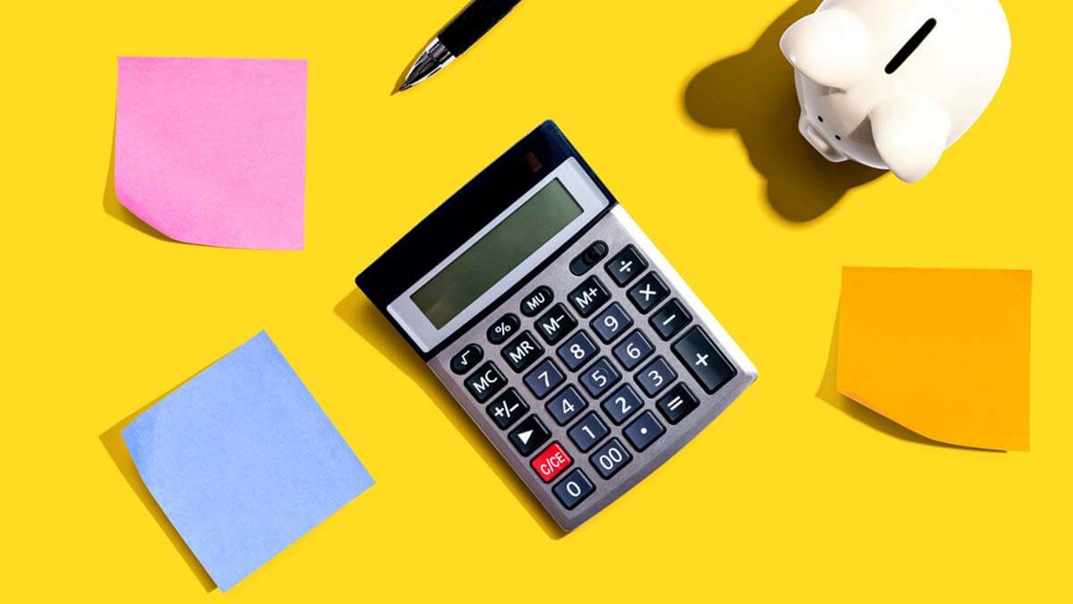 Calculator, post-it notes and piggy bank on a yellow background.