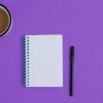 Notebook, pen, and coffee on a purple background.