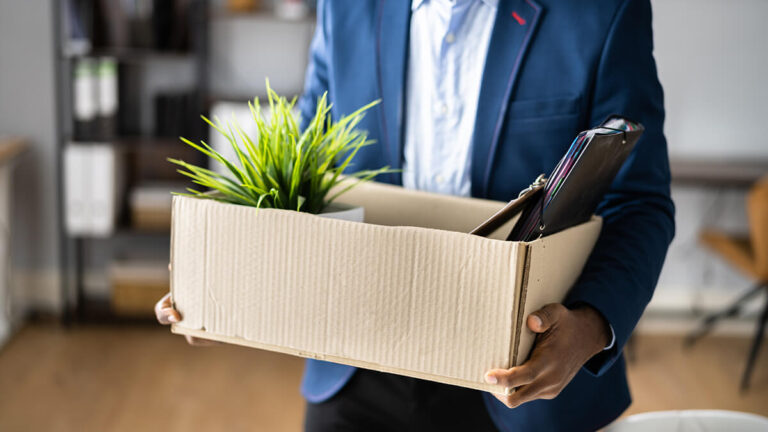 Terminated employee carrying box of belongings out of the office.