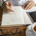 desk with a calendar, cell phone, glasses, and a cup of tea