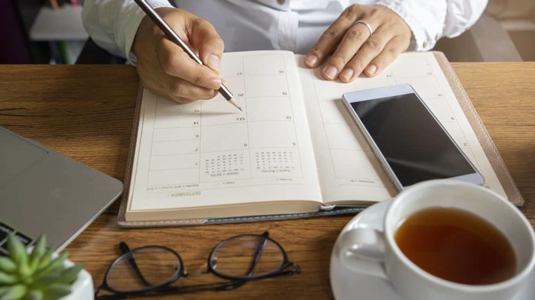 desk with a calendar, cell phone, glasses, and a cup of tea