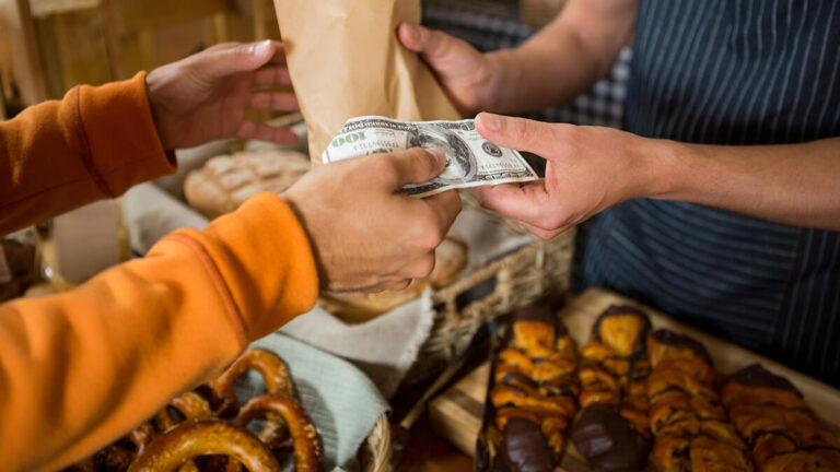 Customer giving $100 bill to a cashier who hands them a brown bag.
