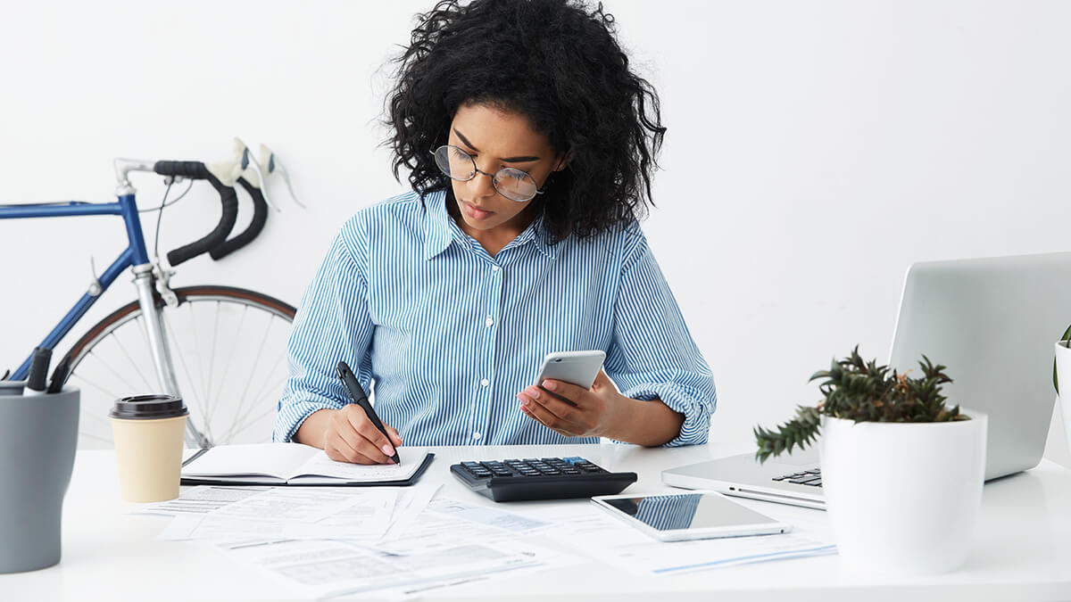 Woman writing in a book and using her cell phone.