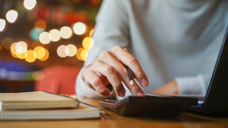 Woman using a calculator. Twinkling lights in the background.