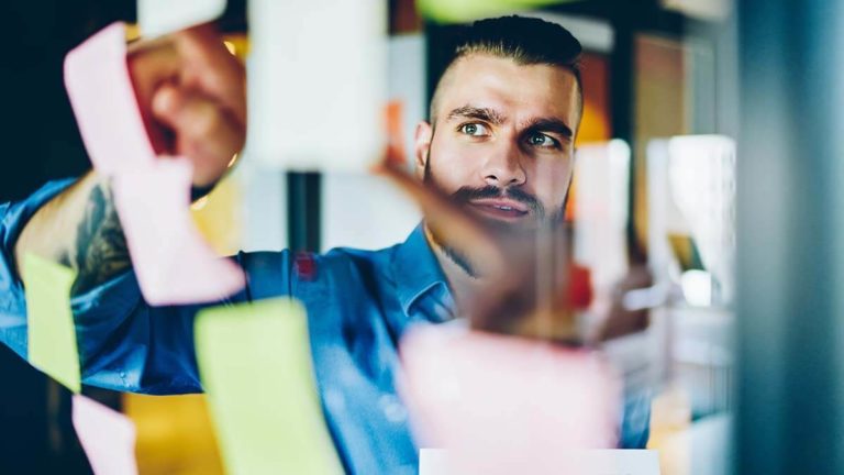 Man pointing to sticky notes on a clear wall.