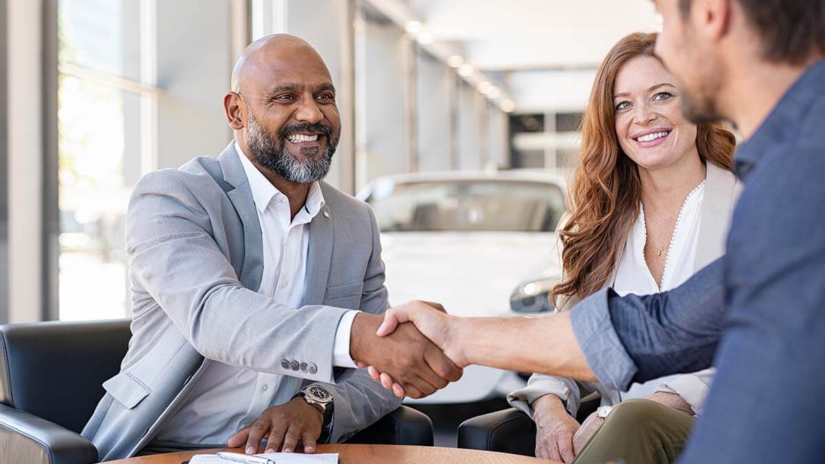 Two men shaking hands next to a smiling woman.