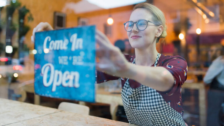 Woman putting up a "Come in we're open" sign.