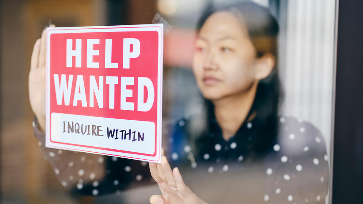 Woman hanging up a "Help Wanted; Inquire Within" sign.