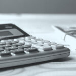 Calculator and stack of bills on a table.