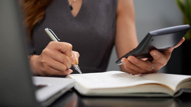 Woman calculating net pay from gross pay with calculator and paper.