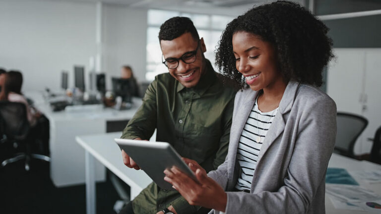 Two co-workers smiling at a tablet.