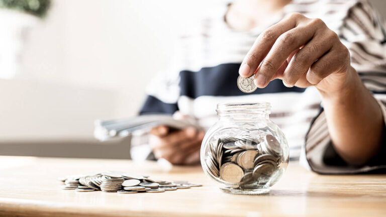 Person dropping coins into a glass jar.