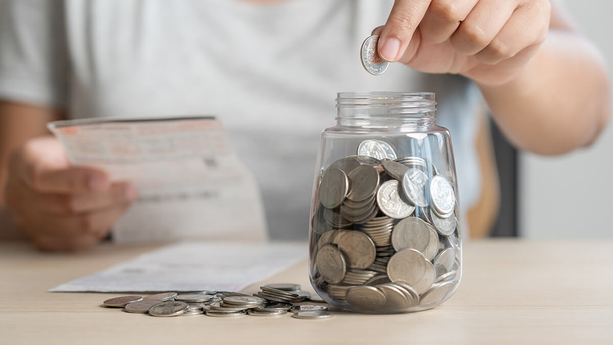 Person dropping coins into a glass jar.