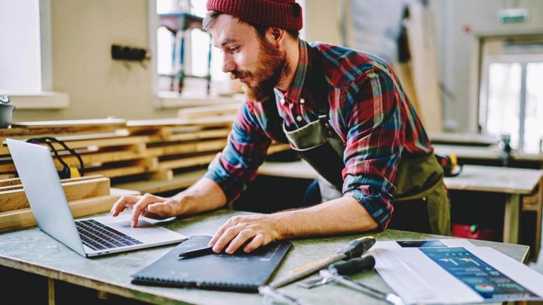 Man working on a laptop in a wood shop.