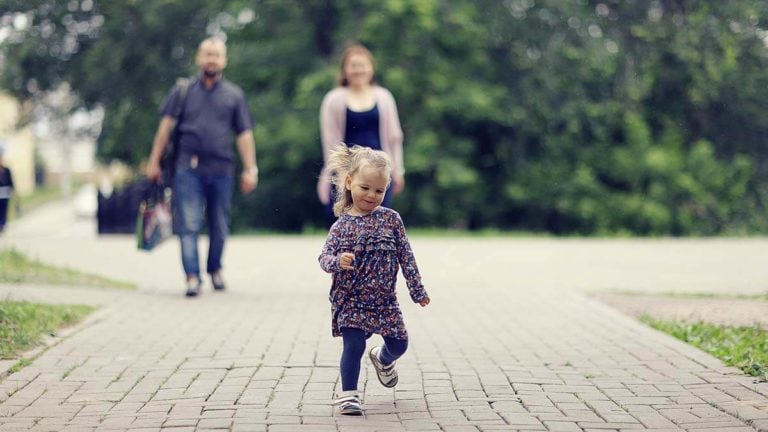 Toddler running in front of parents.