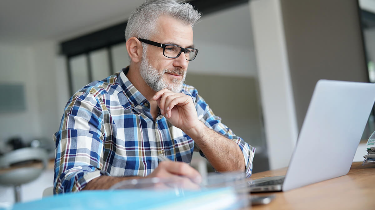 Older man with hand under head looking at a computer.