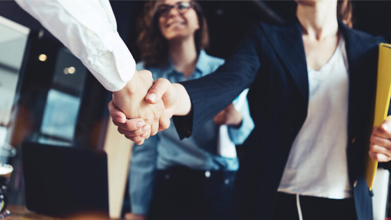 Two people shaking hands while a third smiles in the background.