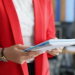 Woman in a red blazer holding a stack of papers.