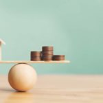 House and coins on a balance ball.