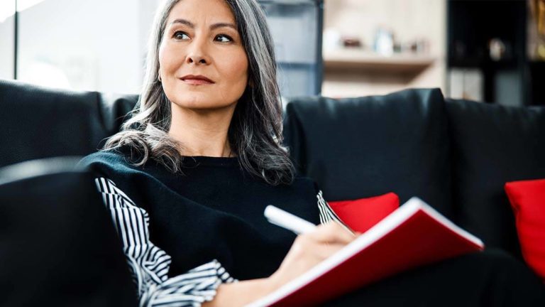 Woman filling out a notebook and looking in the distance.