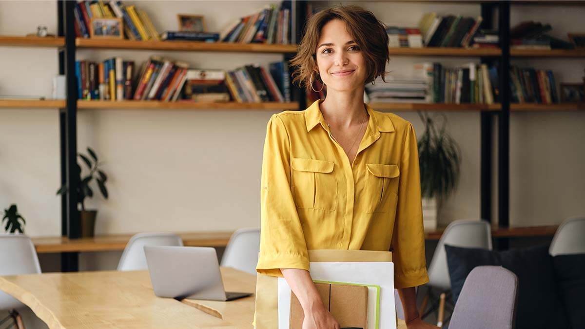 Woman holding paperwork, smiling slightly at the camera.