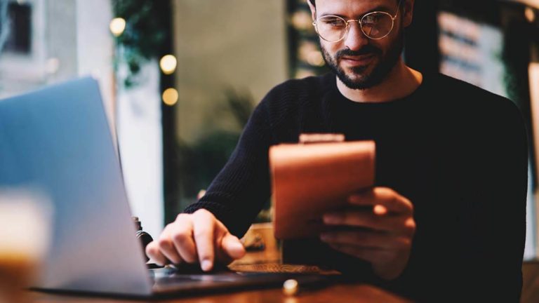 Man with glasses looking at notebook in dimly-lit room.