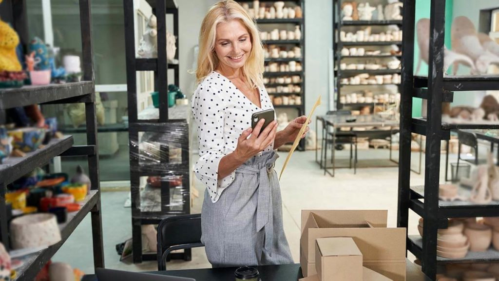 Business owner in her pottery store smiling at her cell phone.