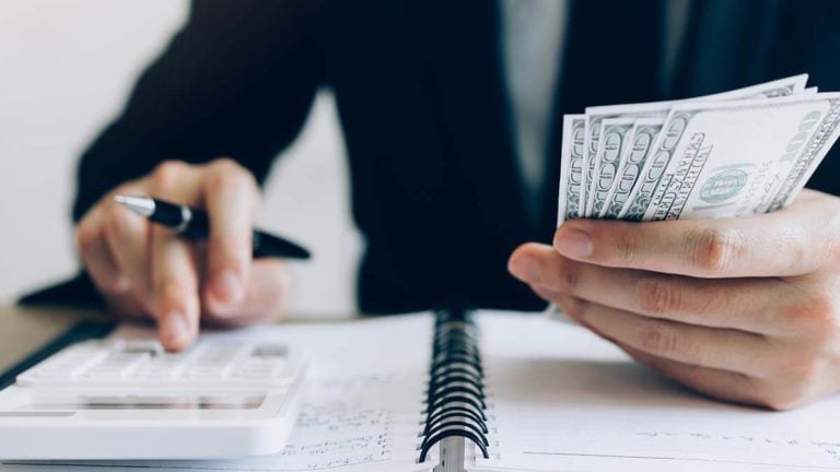Employer holding cash in one hand and using a calculator with the other hand.