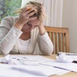 Stressed woman at kitchen table with her hands on her head.