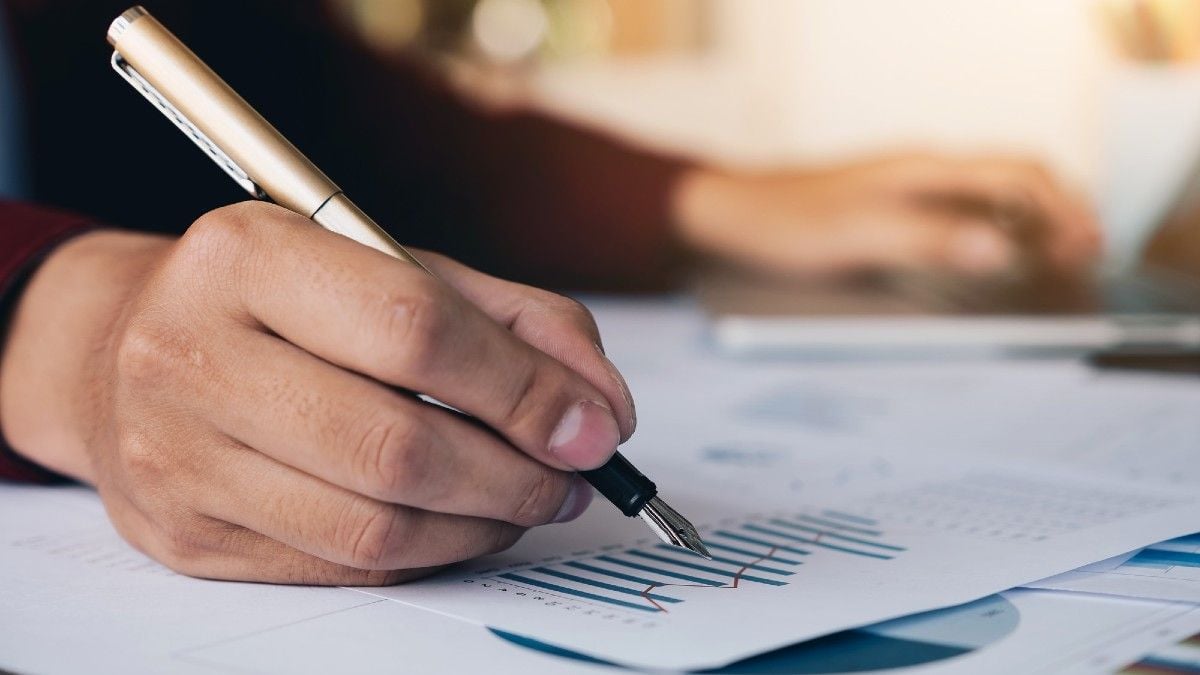 man's hand holding a pen and looking at a graph