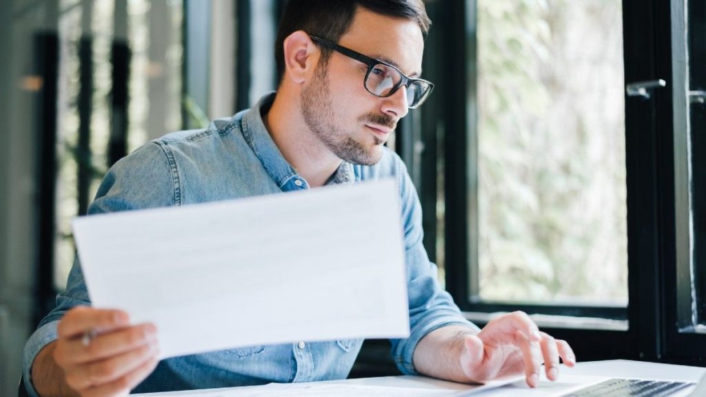 business man in office looking at and working with laptop and income tax return papers and documents