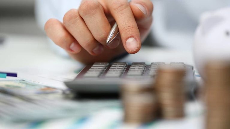 employee typing on a calculator with piles of coins on the table