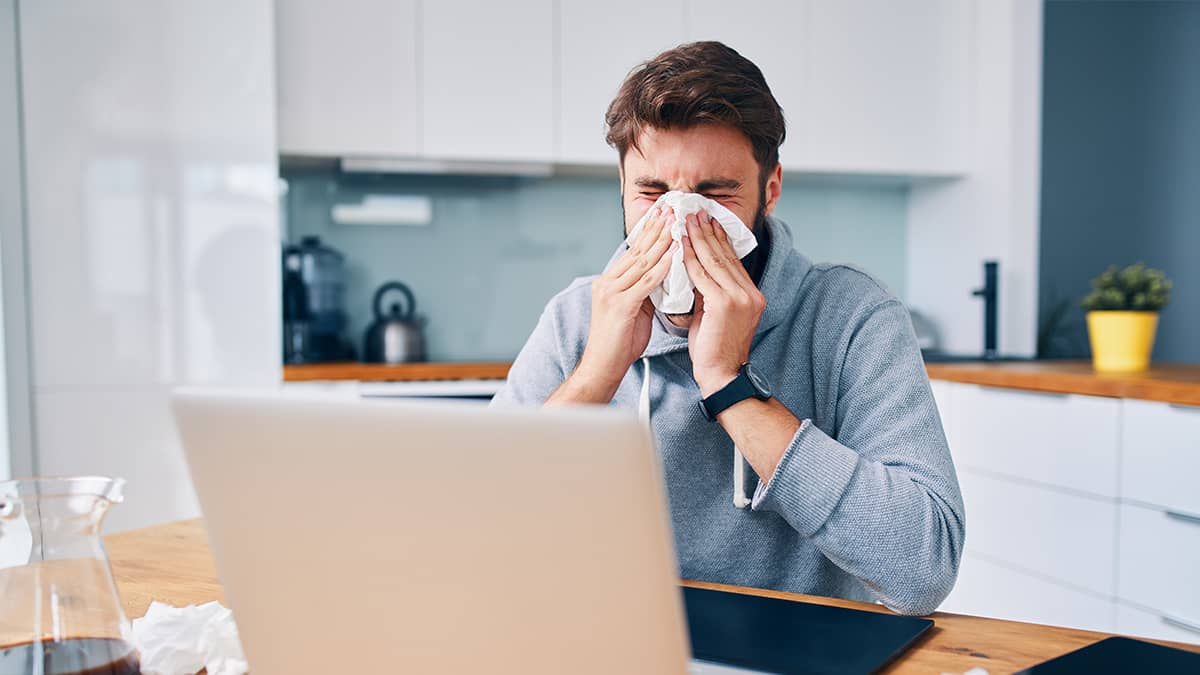 sick man blowing his nose while working from home