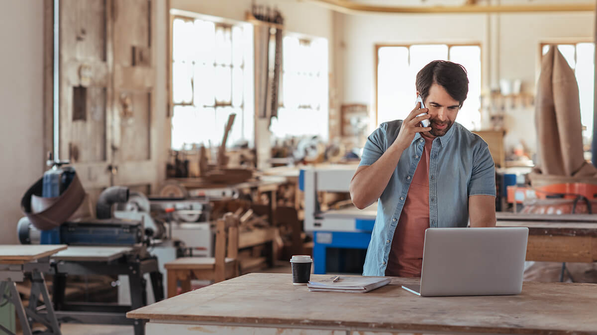 Man on the phone and using a laptop in a work area.