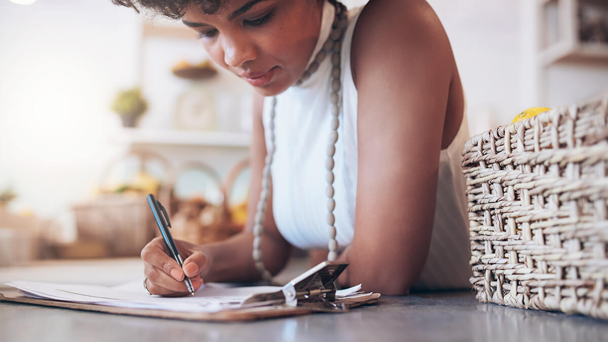 Woman in a sleeveless turtleneck writing at a desk.