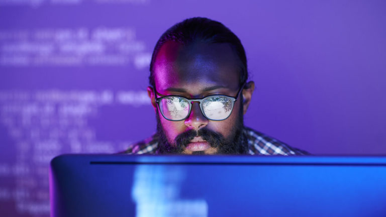 Man looking at data on a computer in a dark room.