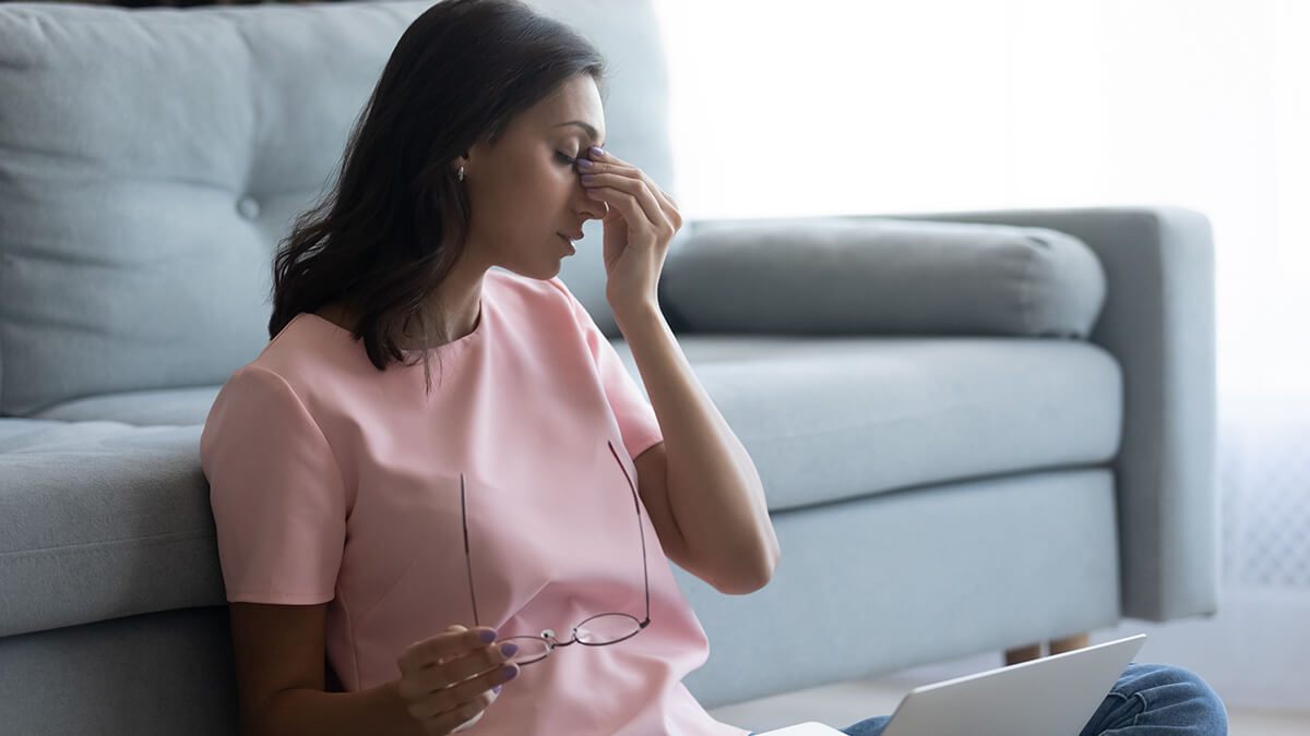 Woman holding glasses in one hand and rubbing the bridge of her nose.