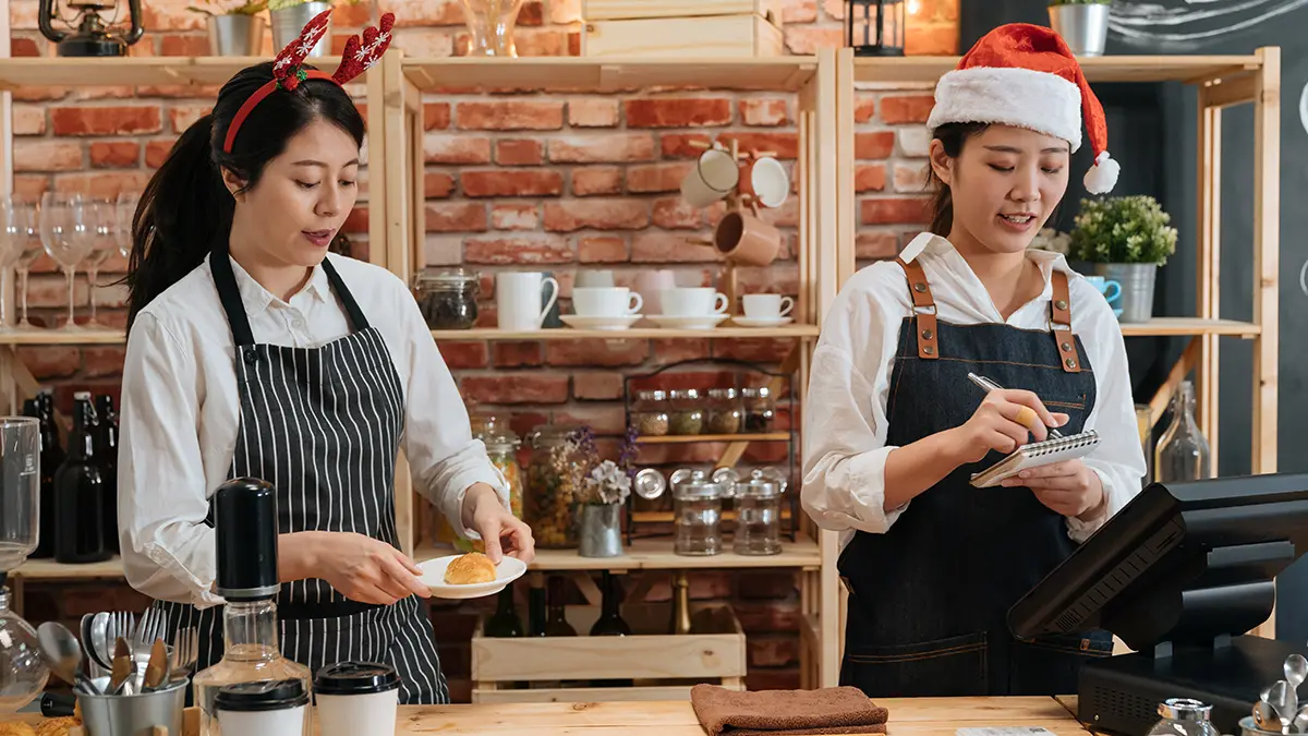 Employees with reindeer antlers and Santa hat working over the holidays at cafe.